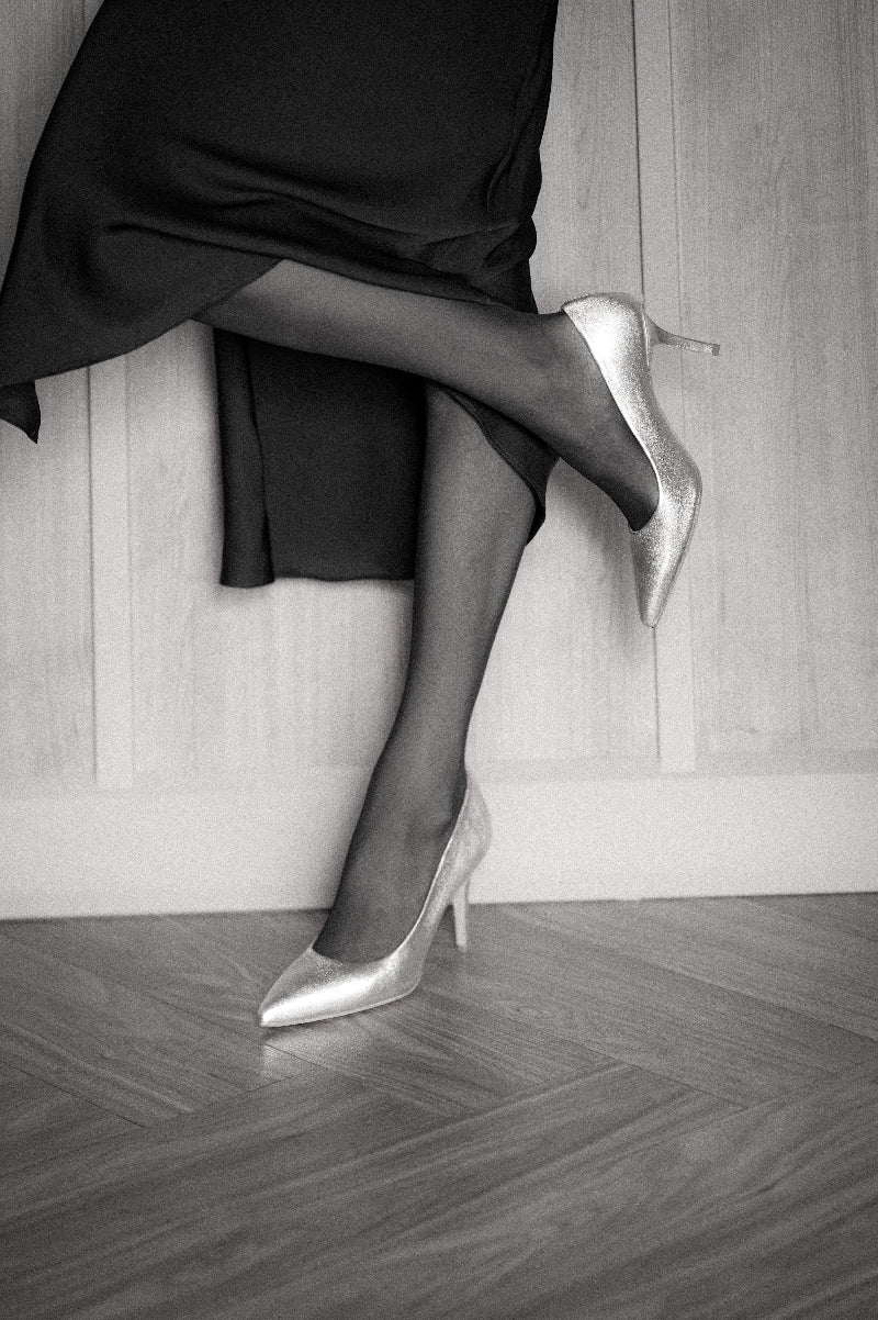 Person wearing black high heels and silver shoes on a wooden floor.