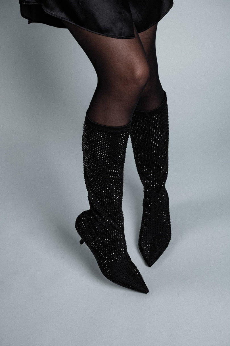 Black knee-high boots with rhinestone details on a plain background