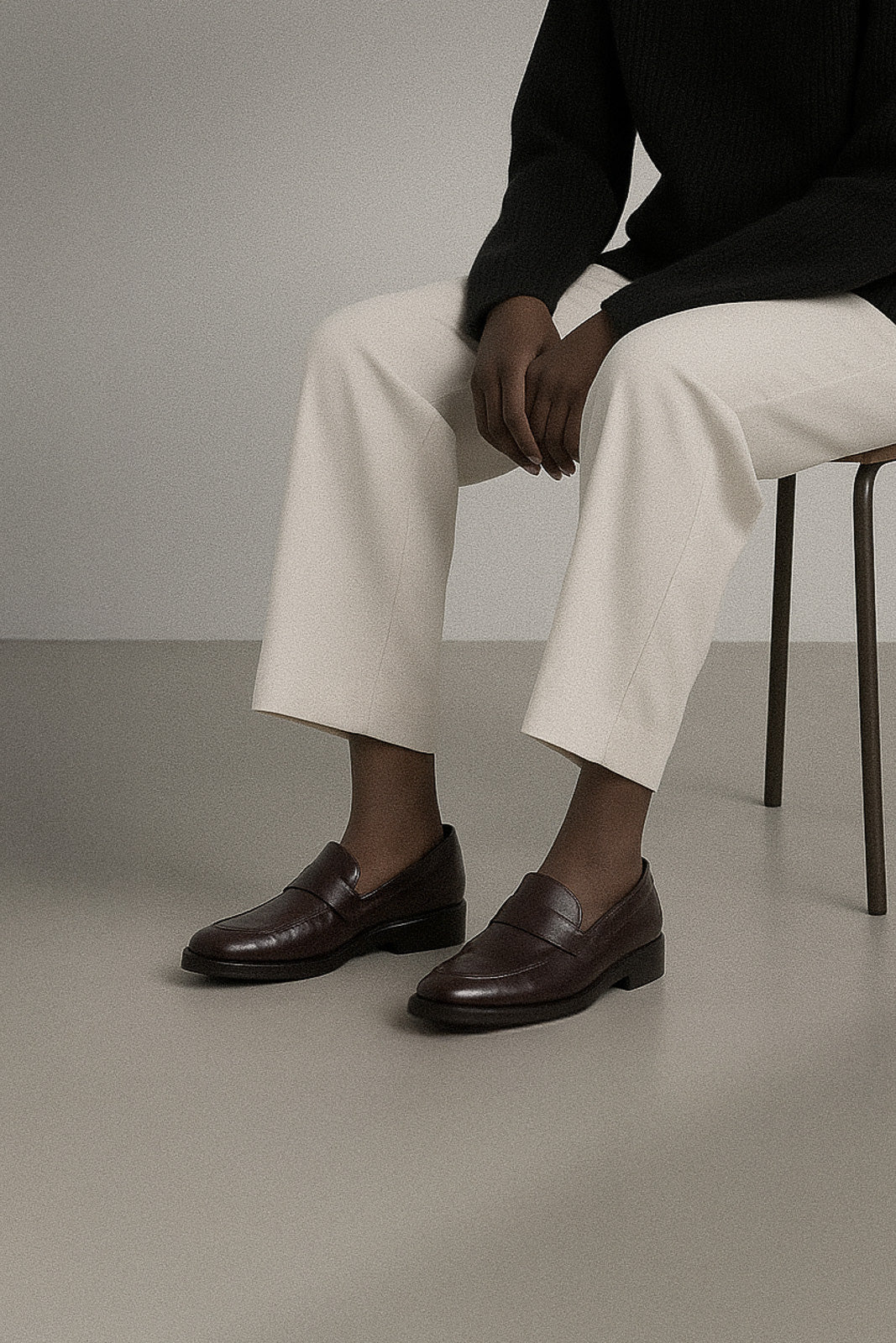 Person wearing brown loafers and white pants sitting on a chair.