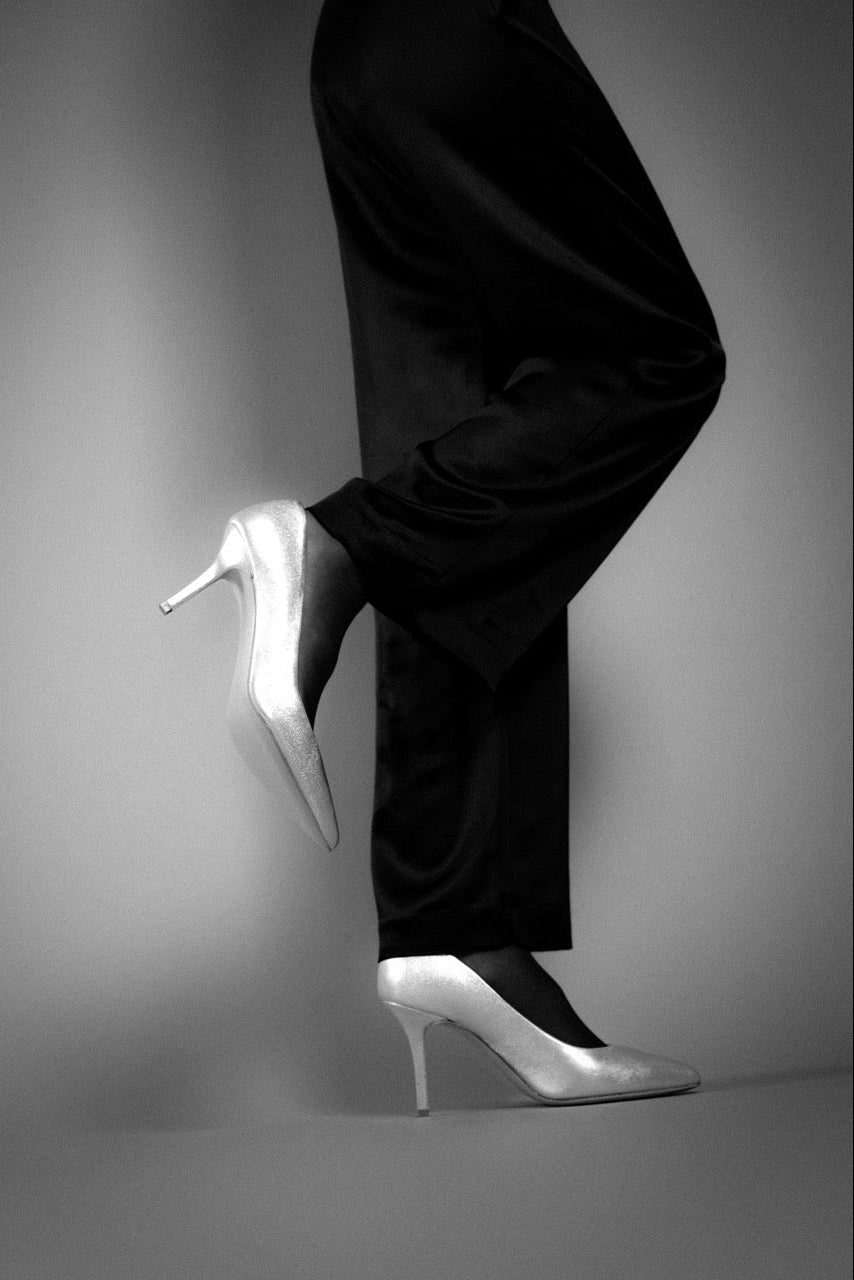 Person wearing black pants and silver high heels on a gray background