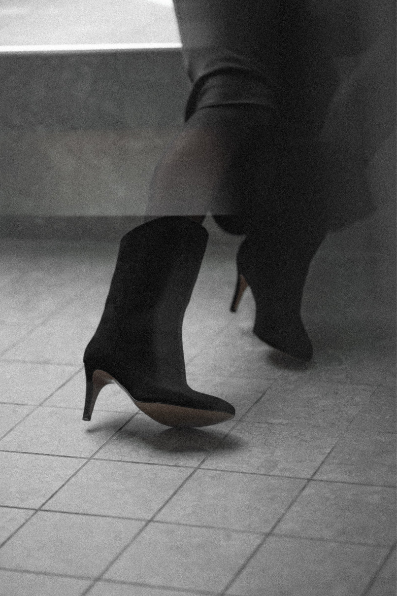 Black suede pumps held by two hands in front of grey wall
