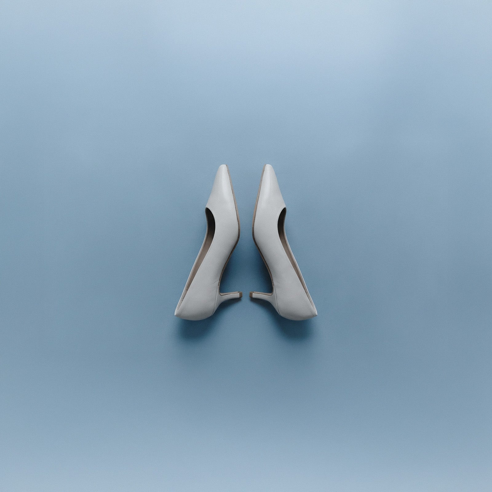 Black suede pumps held by two hands in front of grey wall