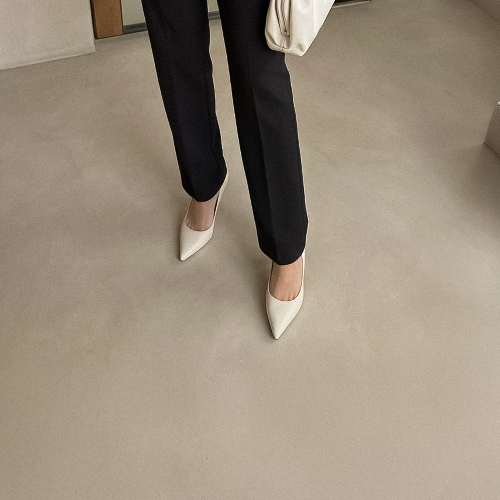 Black suede pumps held by two hands in front of grey wall