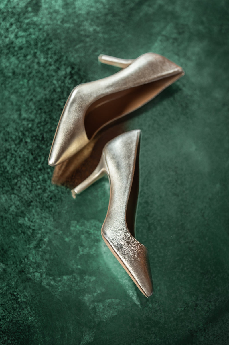 Pair of metallic high-heeled shoes on a textured green surface