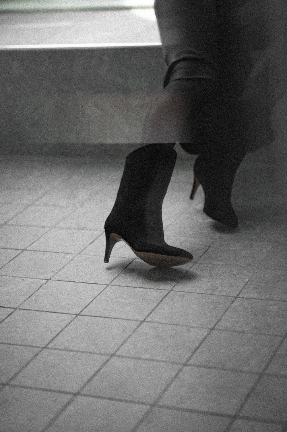 Person wearing black high-heeled boots on a tiled floor