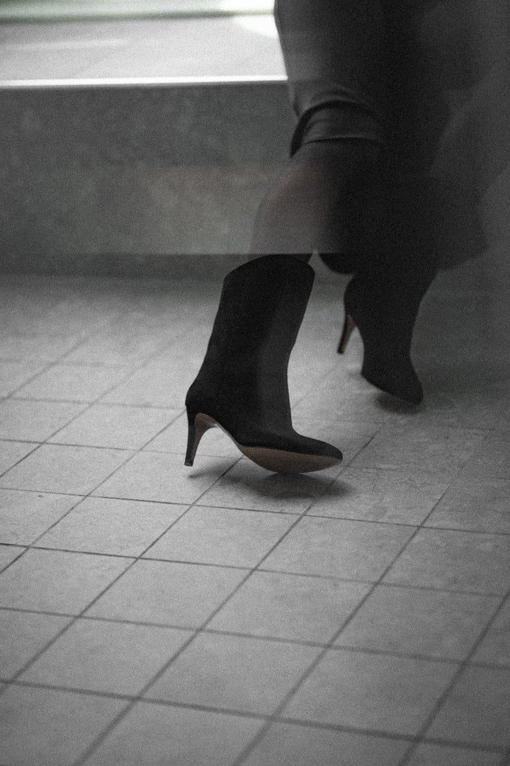 Person wearing black high-heeled boots on a tiled floor