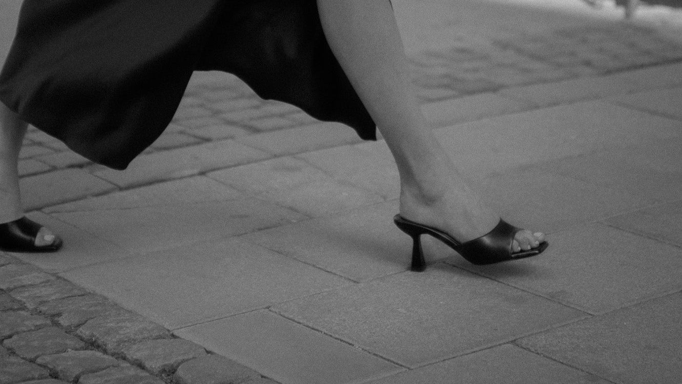 Person in a black dress holding a bag on a sidewalk