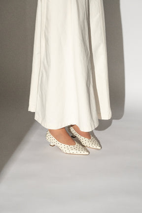 White polka dot shoes worn with a long white skirt on a neutral background