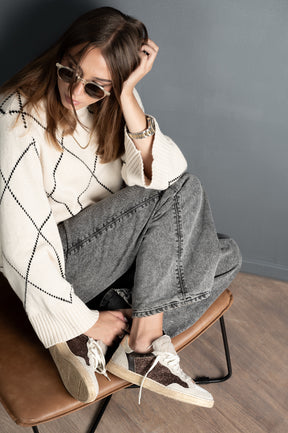Woman sitting on a chair wearing a white sweater, gray jeans, and brown sneakers.