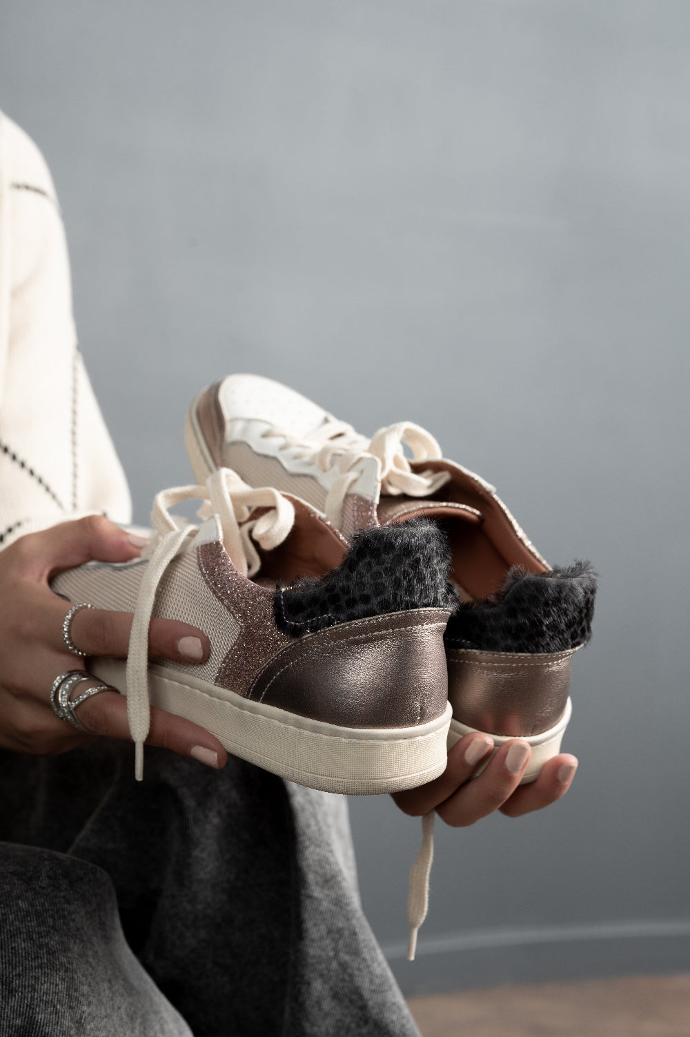 Person holding a pair of brown sneakers with white soles against a gray background
