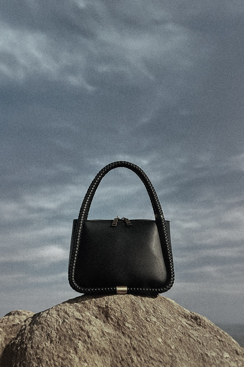 Black handbag on a rock with a cloudy sky background