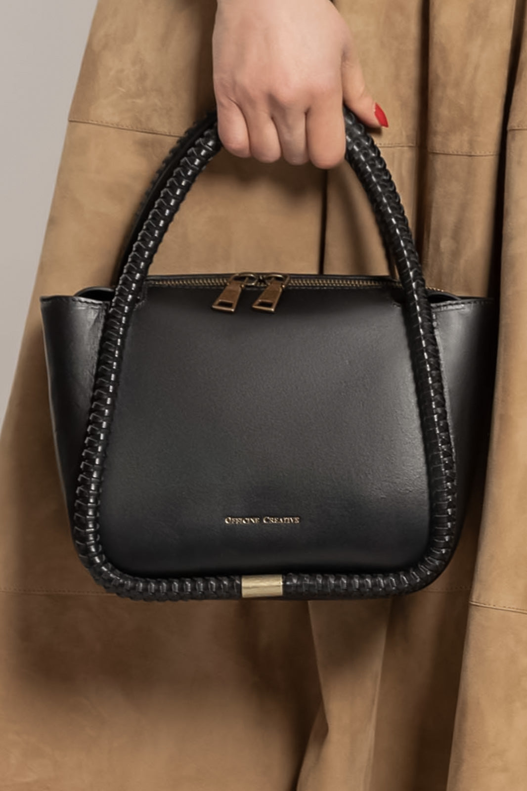 Black handbag with braided handle held by a person wearing a beige coat.