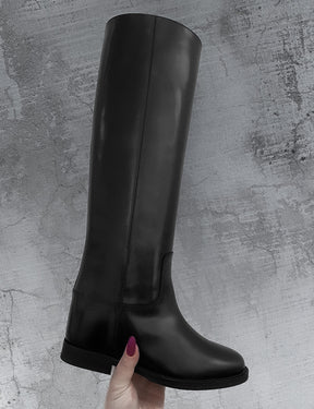 Black knee-high boot held by a hand with purple nail polish on a gray textured background