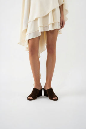 Person wearing a beige dress and brown sandals on a white background