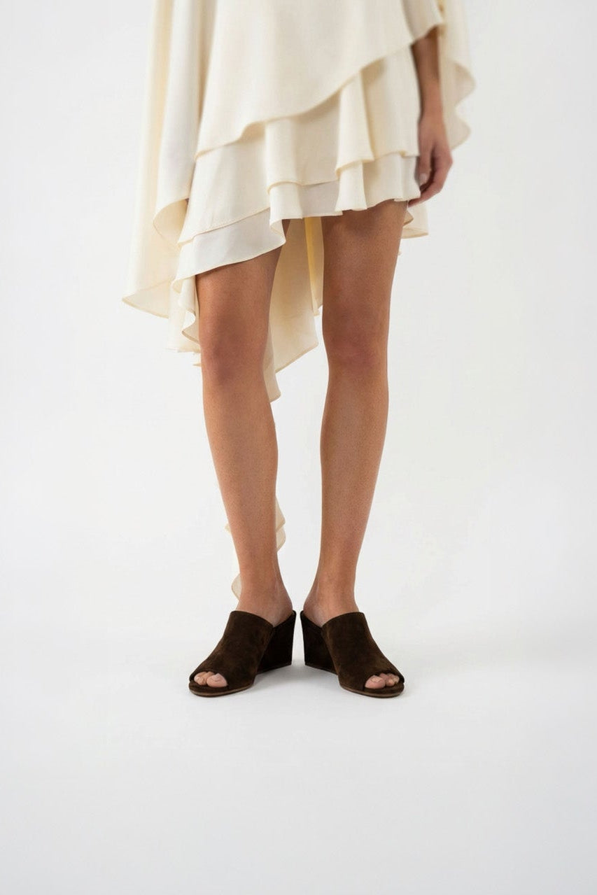 Person wearing a beige dress and brown sandals on a white background