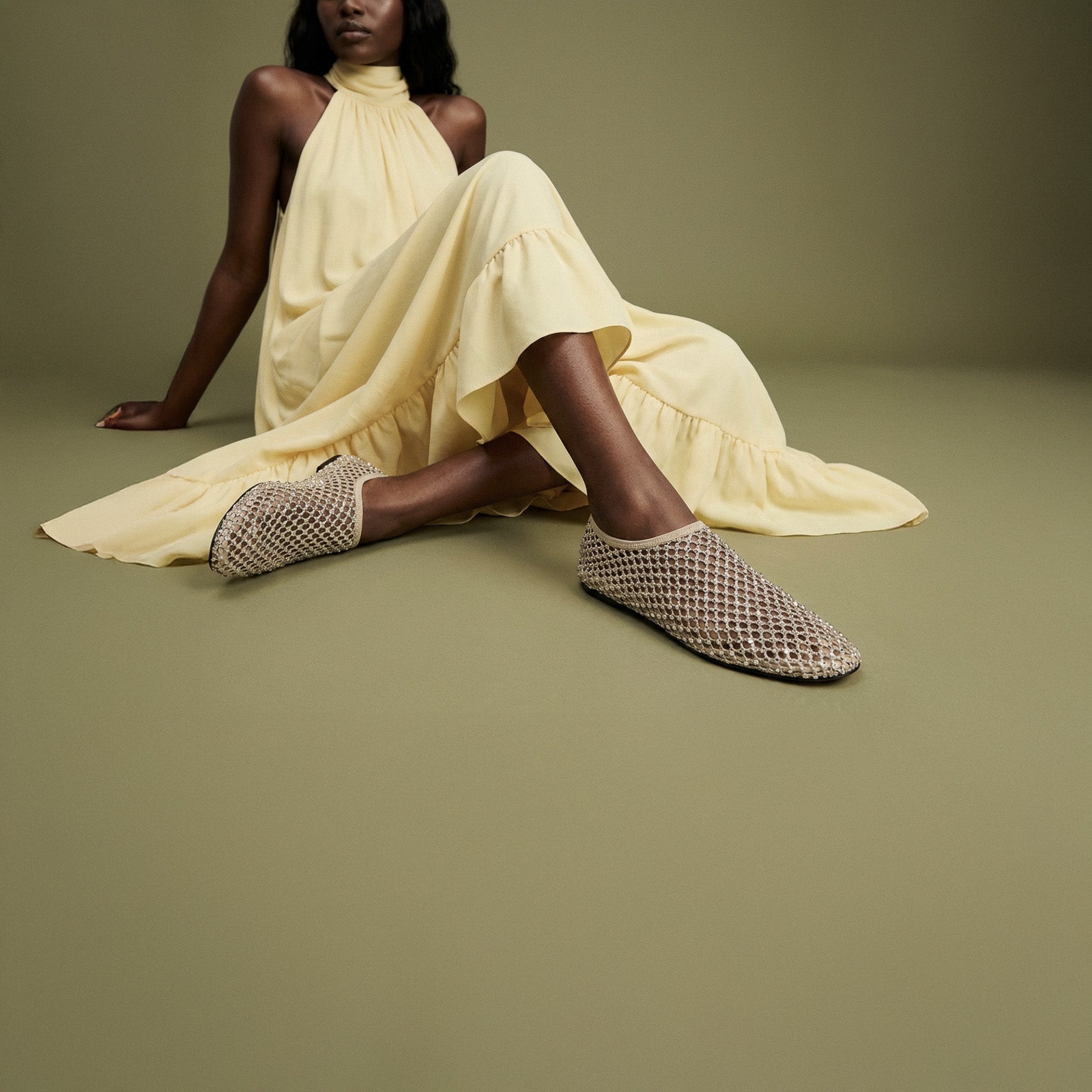 Woman wearing a yellow dress and patterned slippers on a green background
